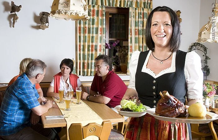 Im Landgasthaus Jägerhof in Absberg zeigt die nette Kellnerin in ihrem feschen Dirndl typische fränkische Speisen: eine Schweinshaxe mit Knödel und Salat. Im Hintergrund warten schön ihre vier hungrigen Gäste.