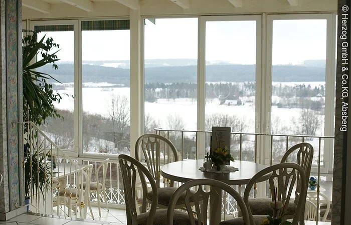 Der schlichte, in weiß gehaltene Innenraum des Cafés Herzog in Absberg. Der Blick geht durch den verglasten Wintergarten nach draußen auf die verschneite Landschaft.