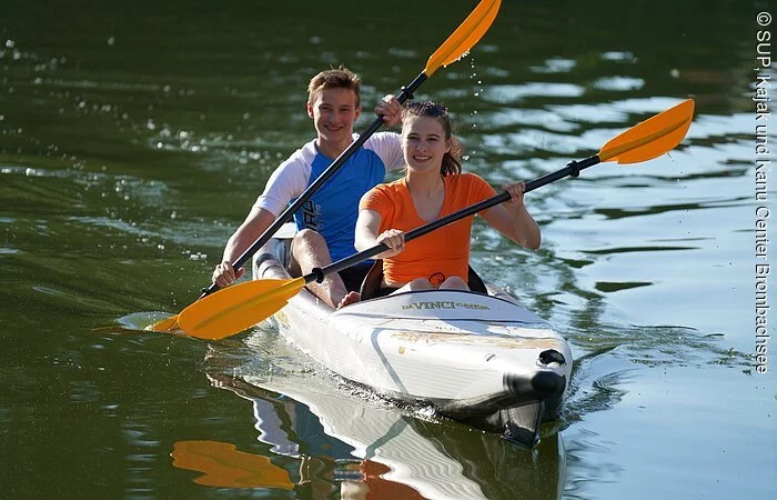 Ein Mädchen und ein Junge paddeln mit ihrem weißen Kanu über das Wasser.