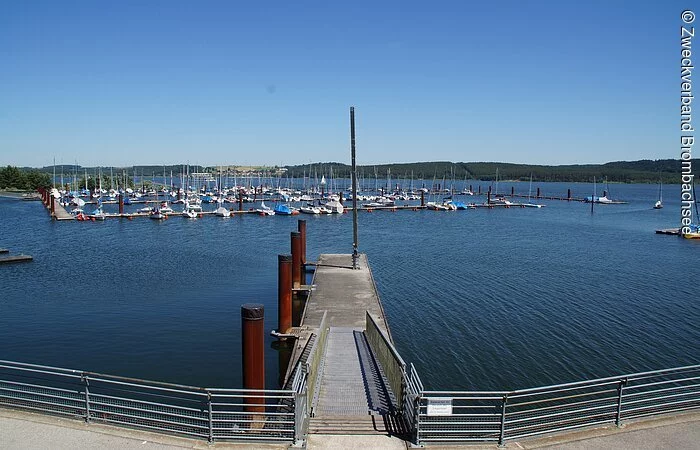 Der Seglhafen am Brombachsee. Ins Wasser führt ein schmaler Steg. Dahinter liegt etwas entfernt der Segelhafen mit vielen Segelbooten.
