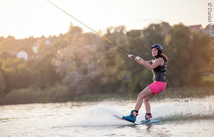 Eine junge Frau gleitet mit ihrem Wakeboard über den See.