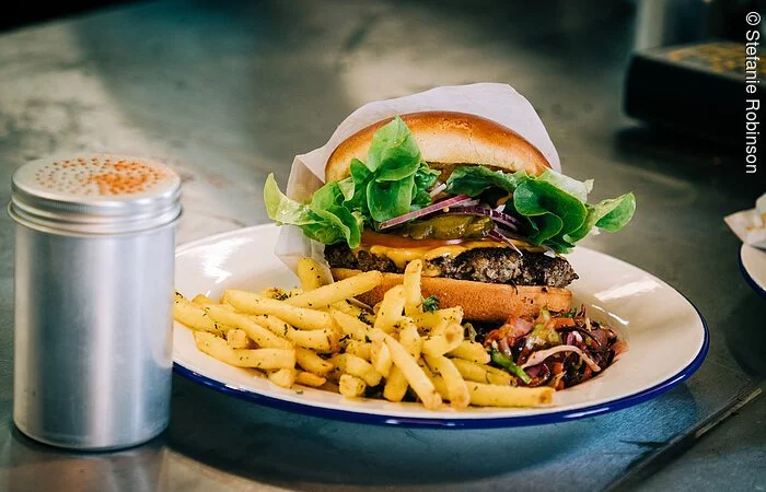 Ein Hamburger mit Pommes auf einem weißen Teller. Der Teller steht auf einer schwarzen Tischplatte.