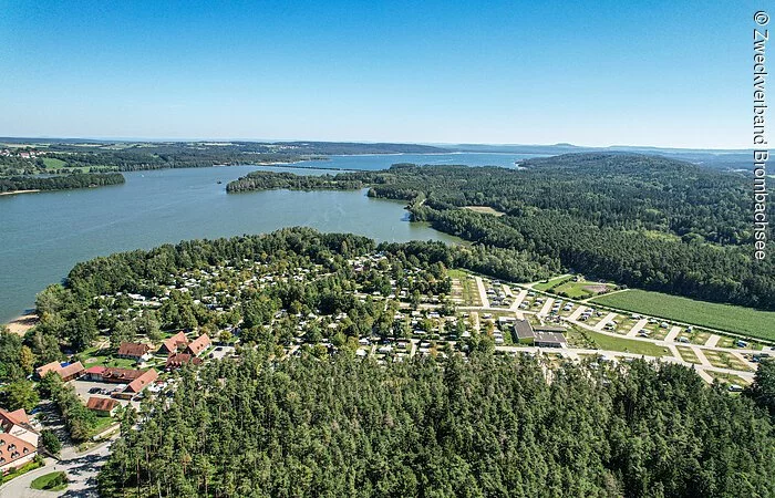 Ein Luftbild des Brombachsees. Der See ist umgeben von Wald. Im vorderen Teil des ein Campingplatz.
