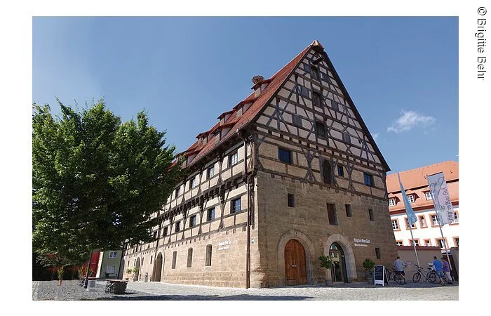 Ein großes Fachwerkhaus mit 6 Ebenen. Die Fassade der unteren zwei Stöcke besteht aus Stein, darüber braunes Fachwerk mit weißer Fassade.